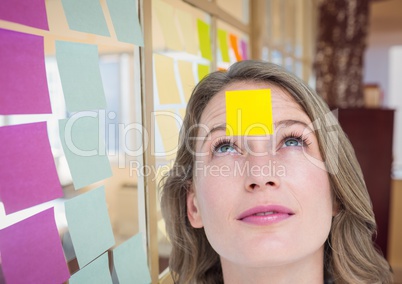 Female executive with sticky note on head in office