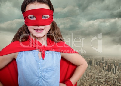 Portrait of super girl wearing red mask and cape standing with hand on hip against cityscape backgro