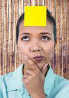 Frustrated woman with sticky note stuck on her forehead against wooden background