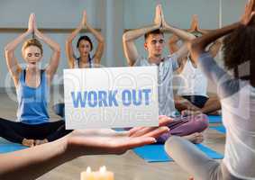 Men and women practicing yoga in fitness studio with hand holding placard in foreground