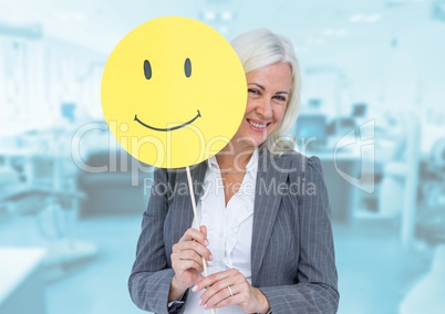 Senior businesswoman holding smiley face against wooden background