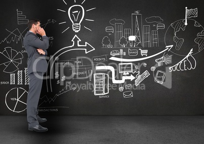 Thoughtful businessman standing against business symbols on blackboard