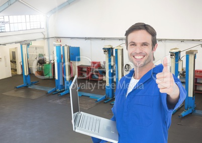 Mechanic with laptop showing thumbs up against garage in background