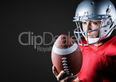 American football player holding rugby ball against black background