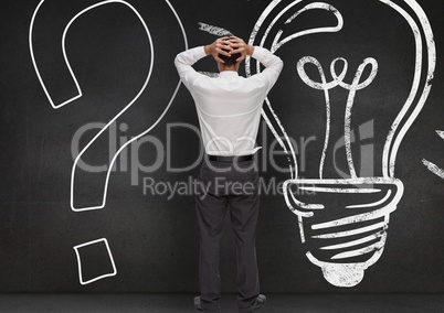 Stressed man standing against question mark and bulb drawn on wooden background