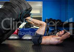 Fit man performing leg press with tire in gym against spiral dots in background