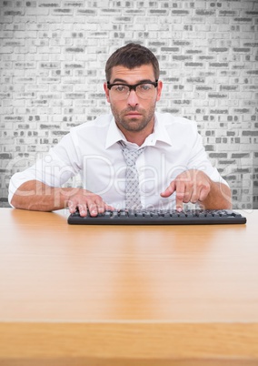 Man in spectacles typing on keyboard against brick wall background