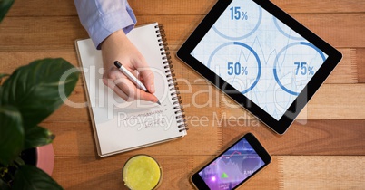Man writing down notes with digital tablet and smartphone on wooden table