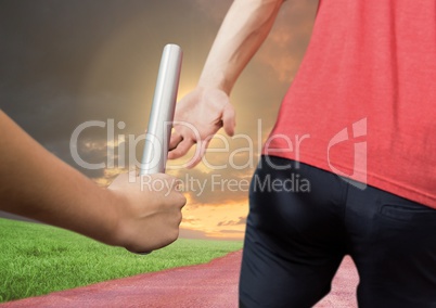 Mid-section of athlete passing the baton to teammate in stadium at sunset