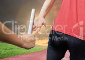 Mid-section of athlete passing the baton to teammate in stadium at sunset