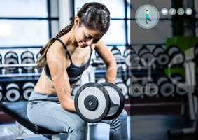 Woman working out with dumb bells against digital interface in gym