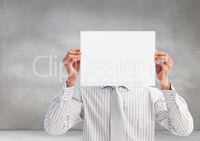 Male executive covering his face behind paper against grey background