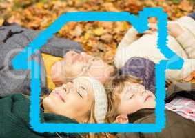 Family relaxing on dry leaves with house model