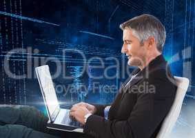 Man sitting on chair using laptop with binary codes in background