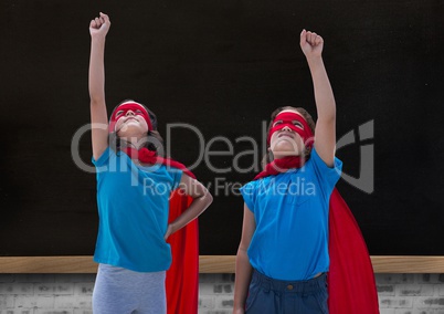 Girls in superhero costume pointing upwards against blackboard in background
