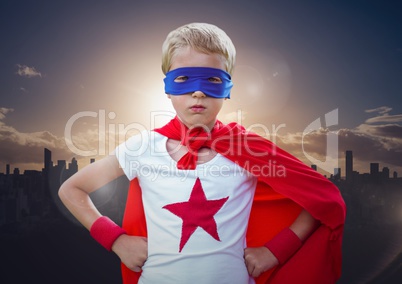 Boy in superhero costume hands on his waist standing against cityscape in background