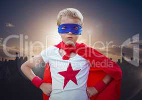 Boy in superhero costume hands on his waist standing against cityscape in background