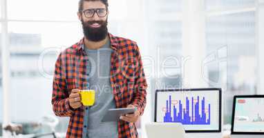 Smiling man using digital tablet while having cup of coffee in office