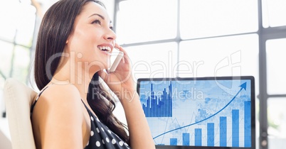 Woman talking on mobile phone against laptop in background