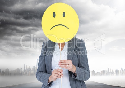Businesswoman holding a smiley face in front of her face with rain clouds in background
