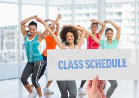 Hand holding placard with class schedule text against women dancing in background