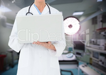 Doctor using laptop against operating room in background