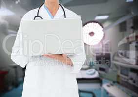 Doctor using laptop against operating room in background