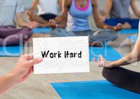 Hand holding placard that reads work hard against people doing meditation