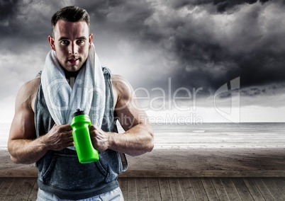 Portrait of muscular man standing with sipper water bottle against storms clouds