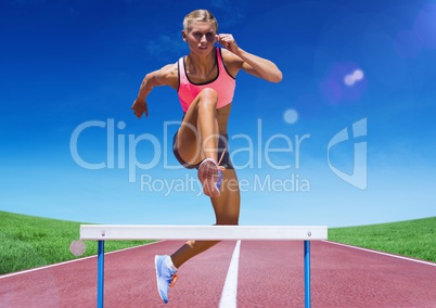 Female athlete jumping over hurdle on race track