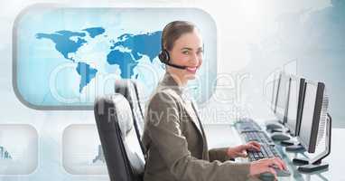 Woman talking on headset and using computer in call centre with world map in background