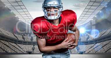 American football player holding rugby ball against stadium in background