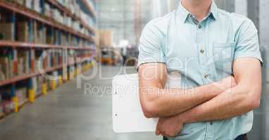 Man standing with arms crossed and holding a clipboard at warehouse