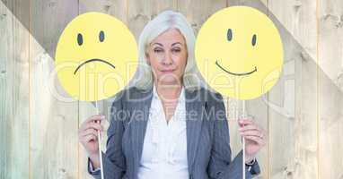 Senior businesswoman holding smiley faces against wooden background
