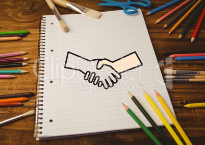 Drawn handshake shape on notebook with color pencils on wooden table