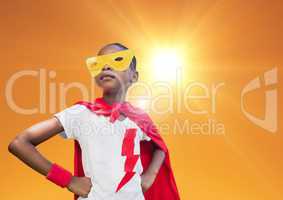 Super kid in red cape and yellow mask standing with hand on hip against bright sunlight