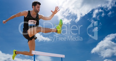 Athlete jumping over hurdles against sky in background