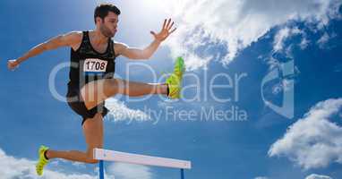 Athlete jumping over hurdles against sky in background