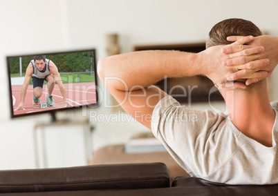 Rear view of man sitting on sofa watching sport channel on tv in living room