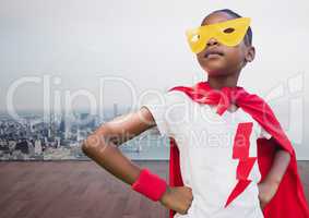 Kid wearing red cape and yellow mask standing with hand on hip against cityscape background