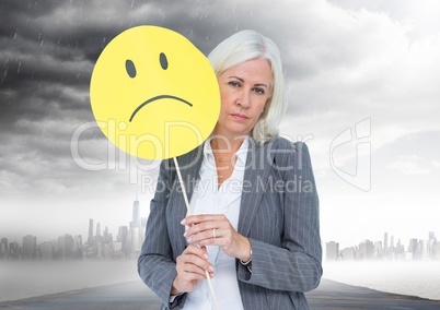 Businesswoman holding a sad face in front of her face with rain clouds in background
