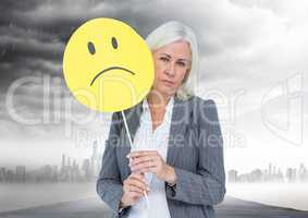 Businesswoman holding a sad face in front of her face with rain clouds in background