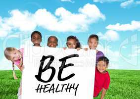Kids holding card showing text  be healthy in front of blue sky and grass