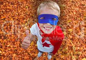 Portrait of smiling kid in red cape and blue mask showing thumbs up during autumn