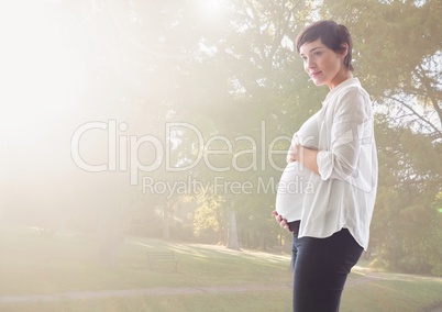 Pregnant woman touching her belly standing against greenery