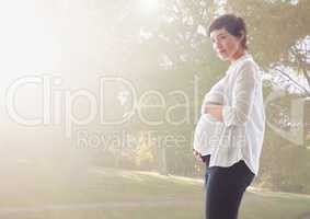 Pregnant woman touching her belly standing against greenery