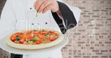 Chef sprinkling herbs on pizza against brick wall background