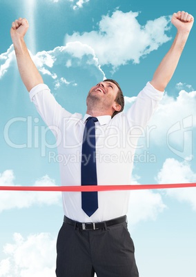 Businessman crossing finish line with arms up against sky and cloud