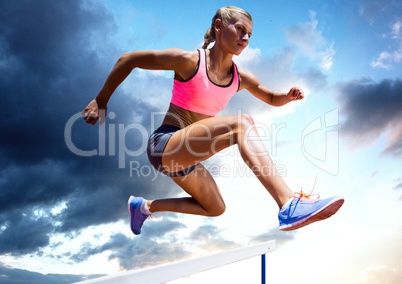 Athlete jumping over a hurdle against sky in background