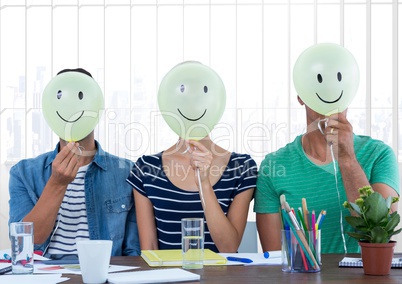 Colleagues holding smiley while sitting on desk